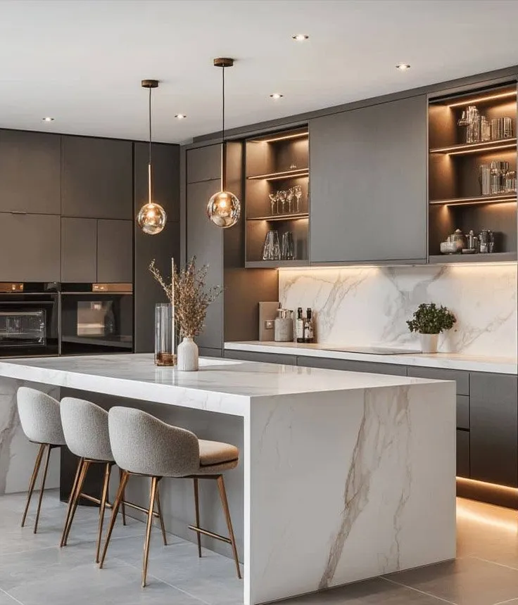 A kitchen in graphite cabinetry with a marble waterfall island, lit open shelving and glass pendants